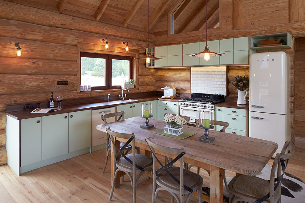 Design ideas for a medium sized rustic l-shaped kitchen/diner in Christchurch with a built-in sink, flat-panel cabinets, green cabinets, wood worktops, white splashback, ceramic splashback, white appliances, light hardwood flooring and no island.