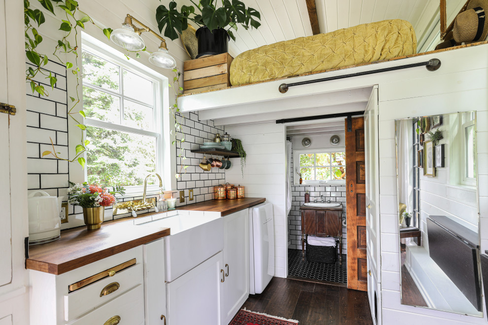 Exempel på ett lantligt brun linjärt brunt kök och matrum, med vita skåp, träbänkskiva, vitt stänkskydd, stänkskydd i tunnelbanekakel, vita vitvaror, mörkt trägolv och brunt golv