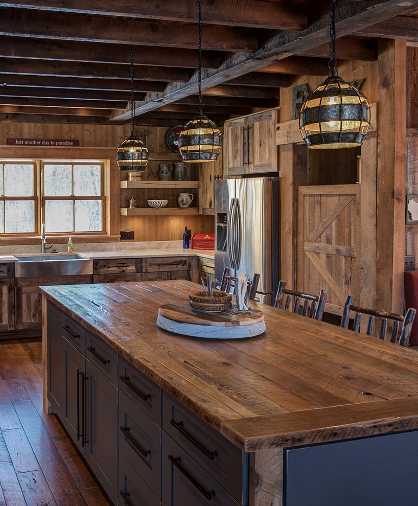 Cette photo montre une cuisine américaine montagne en U et bois vieilli avec un évier de ferme, un placard à porte plane, un plan de travail en quartz, un électroménager en acier inoxydable, îlot et une crédence en bois.