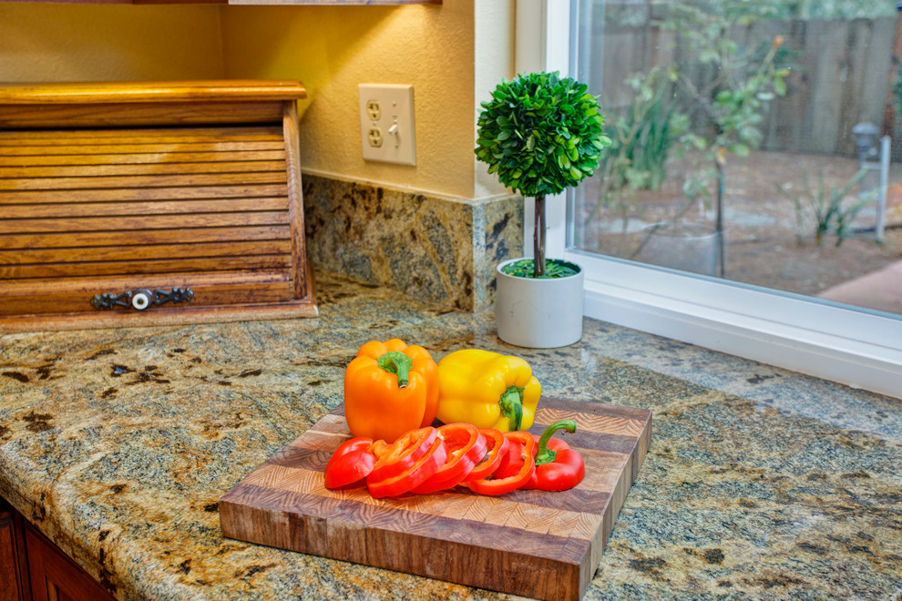 Modelo de cocina tradicional con fregadero bajoencimera, armarios con paneles empotrados, puertas de armario de madera oscura, encimera de granito, salpicadero beige, salpicadero de losas de piedra y electrodomésticos blancos