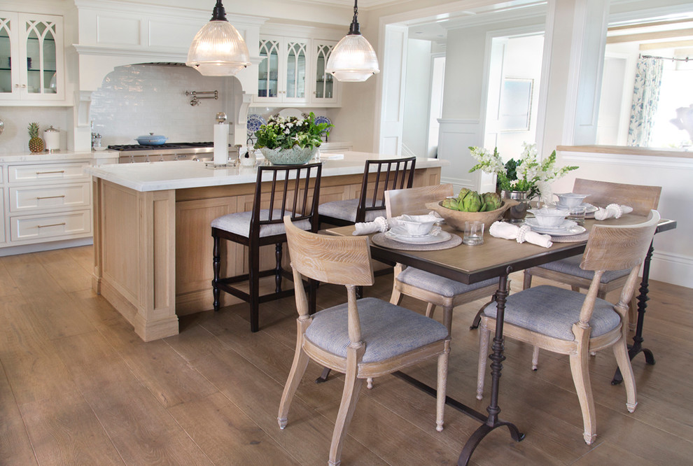 Design ideas for a coastal galley kitchen/diner in Orange County with glass-front cabinets, white cabinets, white splashback, stainless steel appliances and light hardwood flooring.