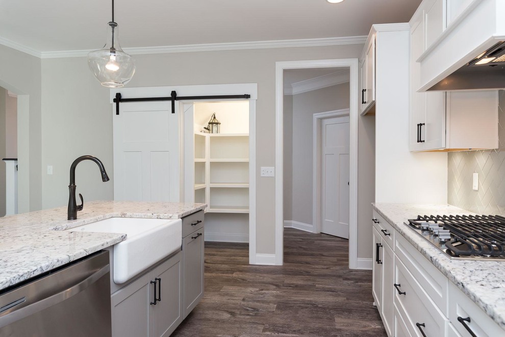 Example of a mid-sized transitional single-wall vinyl floor and brown floor open concept kitchen design in Raleigh with a farmhouse sink, shaker cabinets, white cabinets, granite countertops, gray backsplash, ceramic backsplash, stainless steel appliances and an island