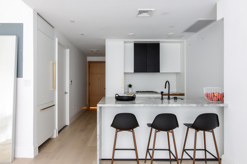 ニューヨークにある北欧スタイルのおしゃれなキッチン (アンダーカウンターシンク、フラットパネル扉のキャビネット、白いキッチンパネル、サブウェイタイルのキッチンパネル、パネルと同色の調理設備、淡色無垢フローリング、ベージュの床、グレーのキッチンカウンター) の写真
