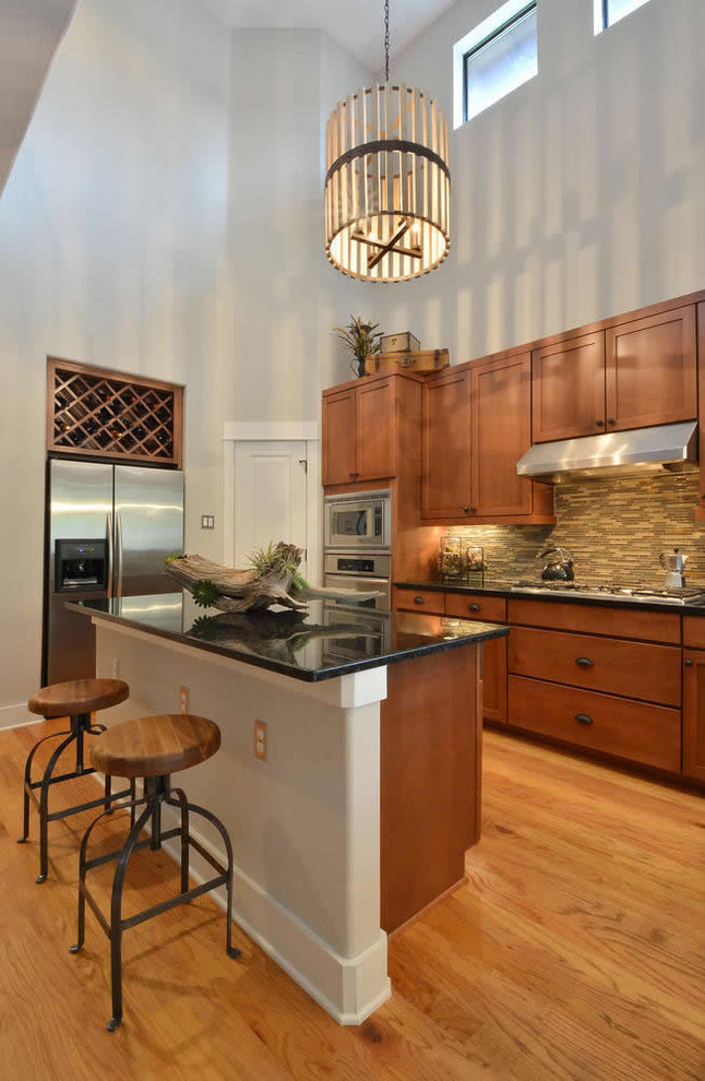 オースティンにある広いインダストリアルスタイルのおしゃれなキッチン (レイズドパネル扉のキャビネット、中間色木目調キャビネット、シルバーの調理設備、淡色無垢フローリング) の写真