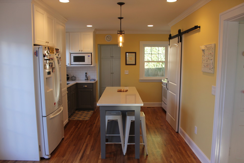 Bild på ett litet lantligt vit vitt kök, med en undermonterad diskho, luckor med infälld panel, vita skåp, bänkskiva i kvarts, vitt stänkskydd, stänkskydd i tunnelbanekakel, vita vitvaror, mellanmörkt trägolv, en köksö och brunt golv