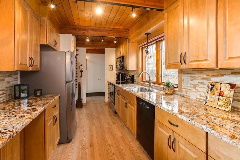 Bild på ett litet vintage kök, med en undermonterad diskho, luckor med upphöjd panel, skåp i mellenmörkt trä, granitbänkskiva, gult stänkskydd, stänkskydd i glaskakel, svarta vitvaror, laminatgolv och en halv köksö
