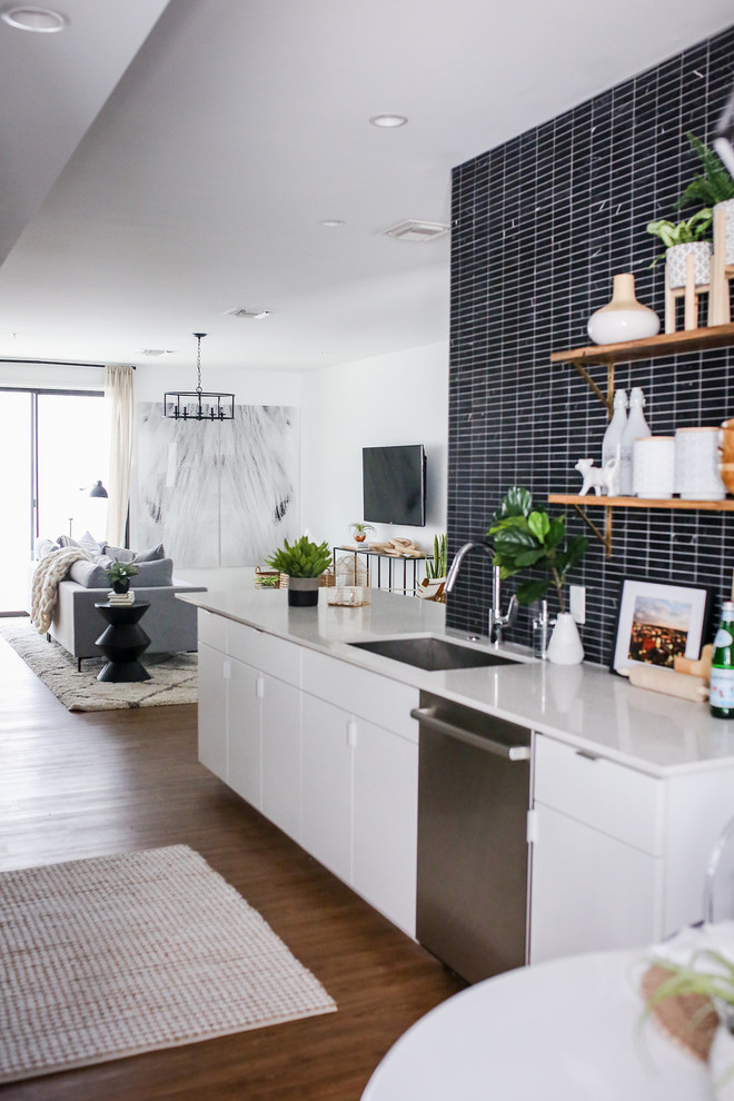 Design ideas for a small scandinavian galley open plan kitchen in Phoenix with a single-bowl sink, flat-panel cabinets, white cabinets, engineered stone countertops, black splashback, marble splashback, stainless steel appliances, vinyl flooring, a breakfast bar and brown floors.