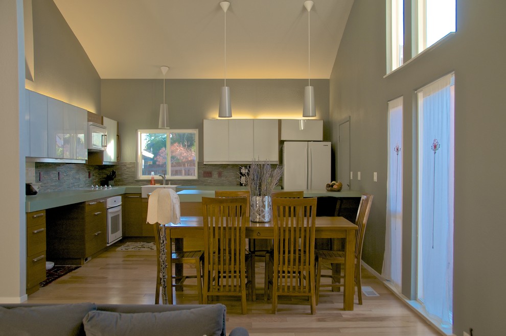 Mid-sized minimalist l-shaped light wood floor eat-in kitchen photo in San Francisco with a farmhouse sink, flat-panel cabinets, solid surface countertops, multicolored backsplash, white appliances, white cabinets, mosaic tile backsplash and no island