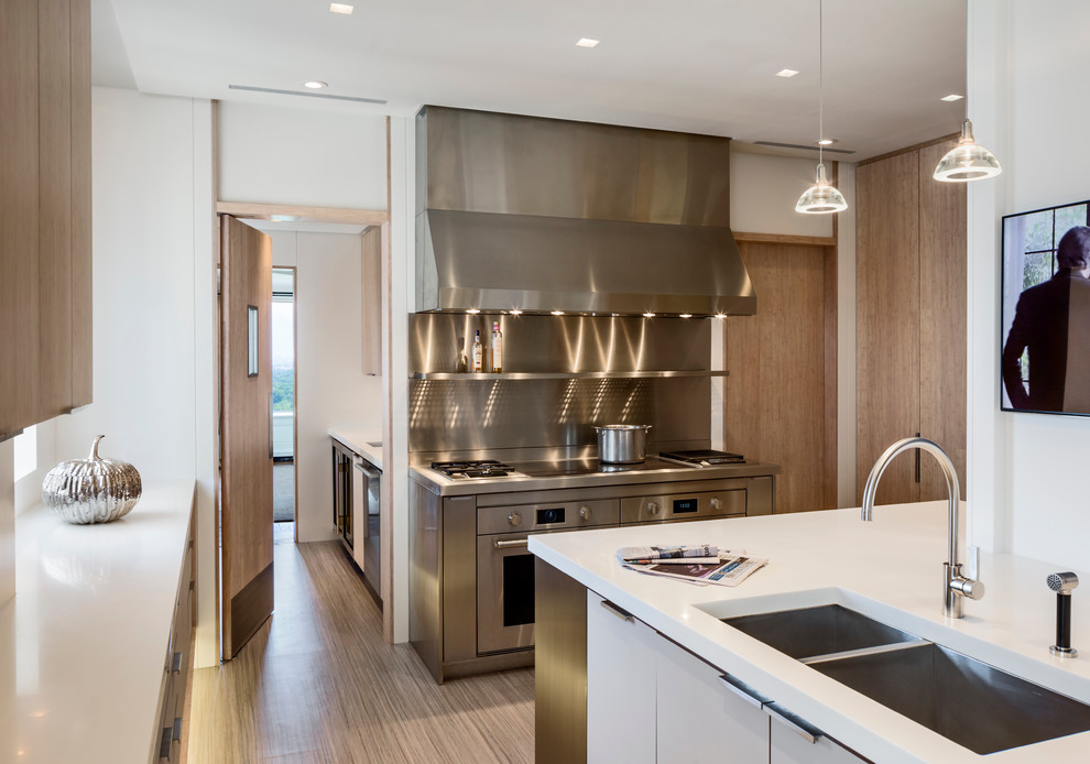 Immagine di una cucina minimalista di medie dimensioni con lavello sottopiano, ante in legno chiaro, top in superficie solida, paraspruzzi bianco e elettrodomestici in acciaio inossidabile