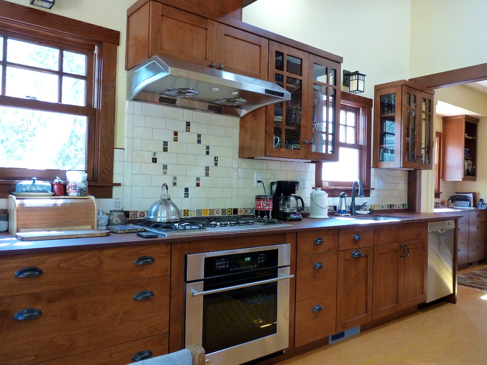 Bild på ett stort amerikanskt kök, med en undermonterad diskho, skåp i shakerstil, skåp i mellenmörkt trä, vitt stänkskydd, stänkskydd i keramik, rostfria vitvaror, korkgolv och en halv köksö