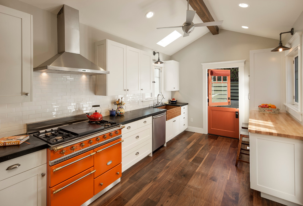 Modelo de cocina de estilo americano pequeña abierta con electrodomésticos blancos, fregadero sobremueble, puertas de armario blancas, encimera de esteatita, suelo de madera oscura y barras de cocina