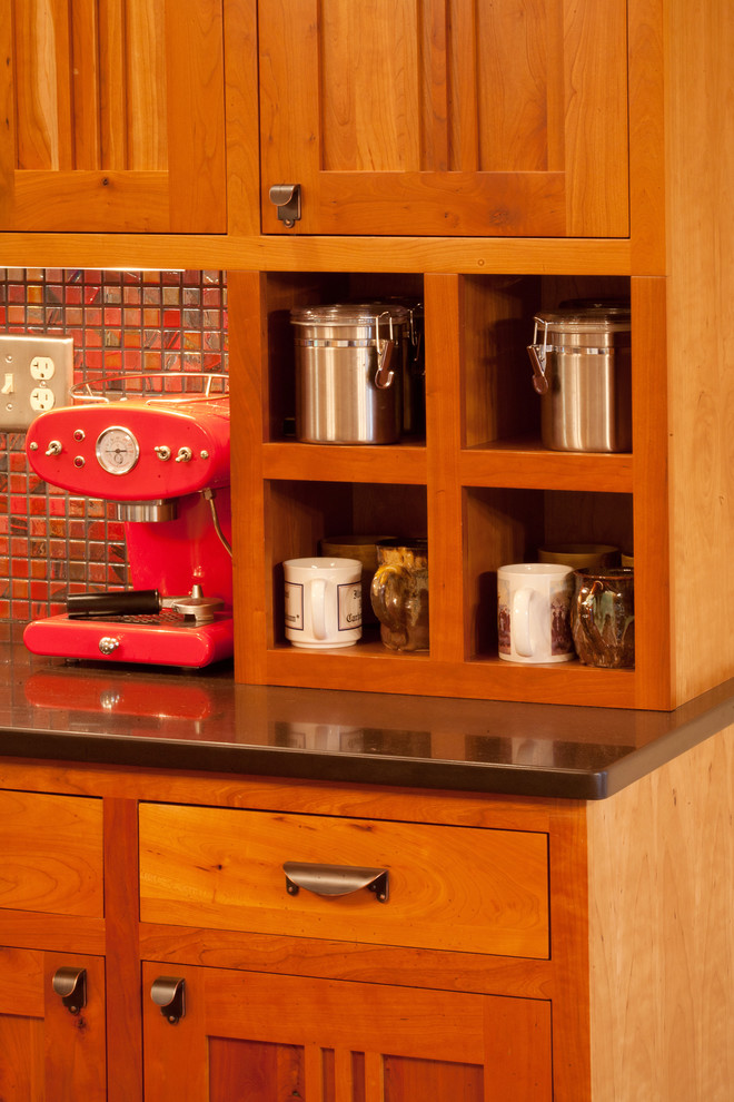 Cette image montre une cuisine américaine traditionnelle en L et bois brun avec un évier encastré, un placard à porte shaker, un plan de travail en quartz modifié, une crédence rouge et un électroménager en acier inoxydable.