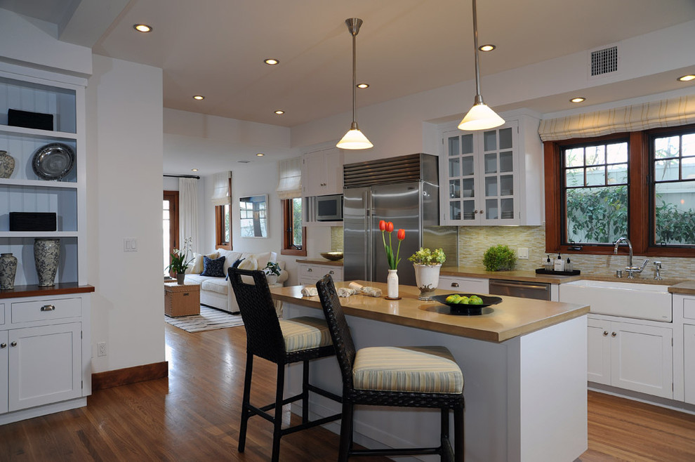 Example of a transitional kitchen design in Los Angeles with a farmhouse sink, glass-front cabinets, white cabinets, concrete countertops, beige backsplash, matchstick tile backsplash and stainless steel appliances