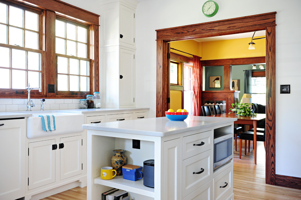 Amerikansk inredning av ett avskilt, mellanstort vit vitt kök, med en rustik diskho, luckor med profilerade fronter, vita skåp, bänkskiva i kvarts, vitt stänkskydd, stänkskydd i keramik, rostfria vitvaror, mellanmörkt trägolv, en köksö och brunt golv