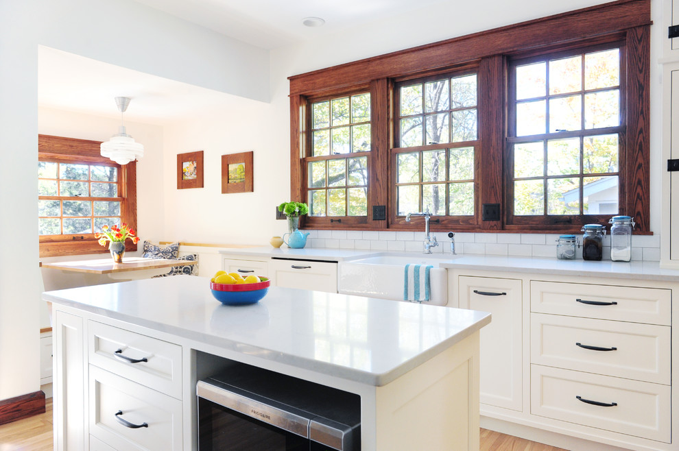 Example of a mid-sized arts and crafts medium tone wood floor and brown floor enclosed kitchen design in Indianapolis with a farmhouse sink, beaded inset cabinets, white cabinets, quartz countertops, white backsplash, ceramic backsplash, stainless steel appliances, an island and white countertops