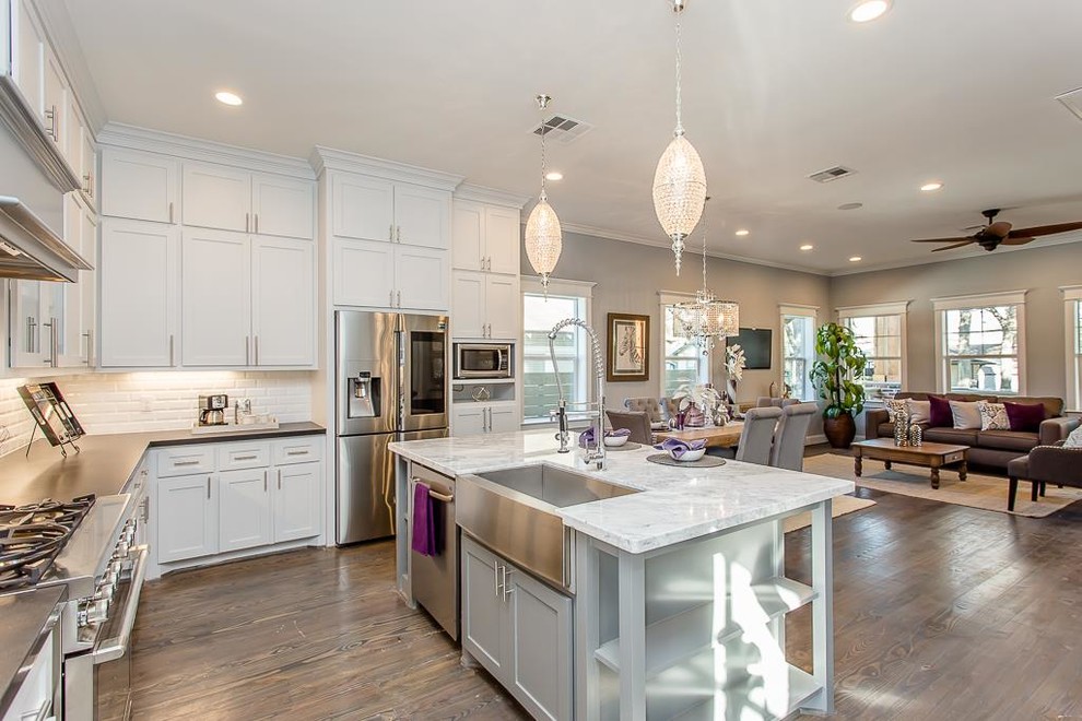 Large arts and crafts l-shaped dark wood floor and brown floor eat-in kitchen photo in Houston with a farmhouse sink, recessed-panel cabinets, white cabinets, quartzite countertops, white backsplash, subway tile backsplash, stainless steel appliances, an island and white countertops