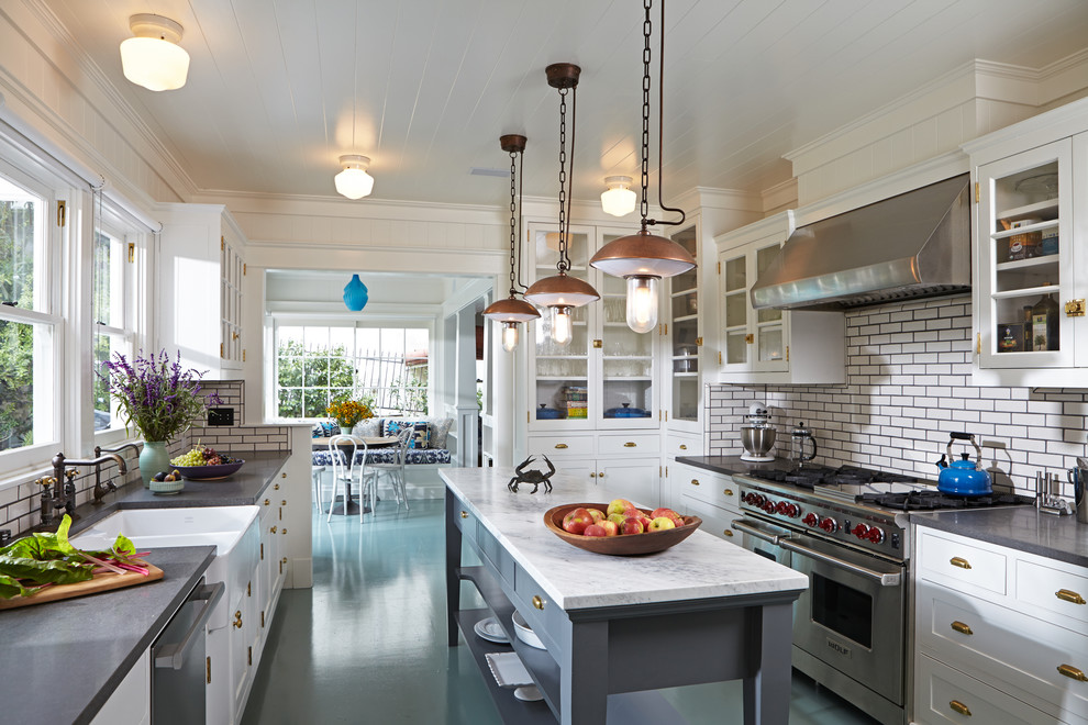 Example of a classic kitchen design in Los Angeles with a farmhouse sink, glass-front cabinets, white cabinets, white backsplash, subway tile backsplash, stainless steel appliances and an island