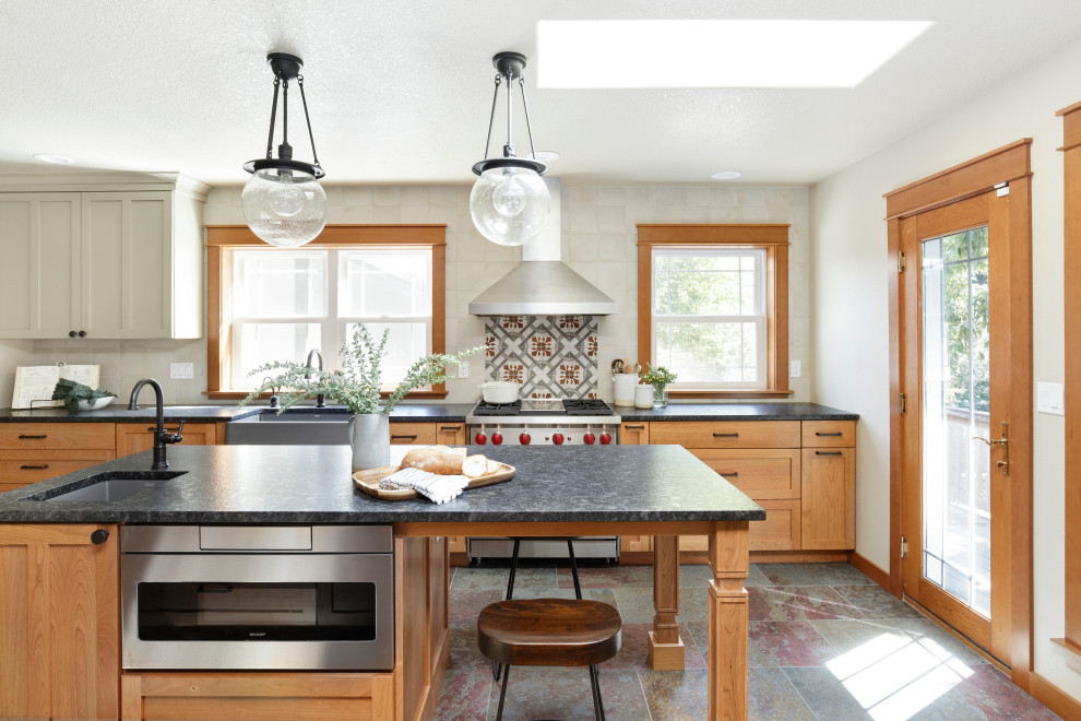 Exempel på ett avskilt, mellanstort lantligt svart svart u-kök, med en rustik diskho, skåp i shakerstil, skåp i mellenmörkt trä, vitt stänkskydd, rostfria vitvaror, en köksö, granitbänkskiva, stänkskydd i keramik, skiffergolv och flerfärgat golv