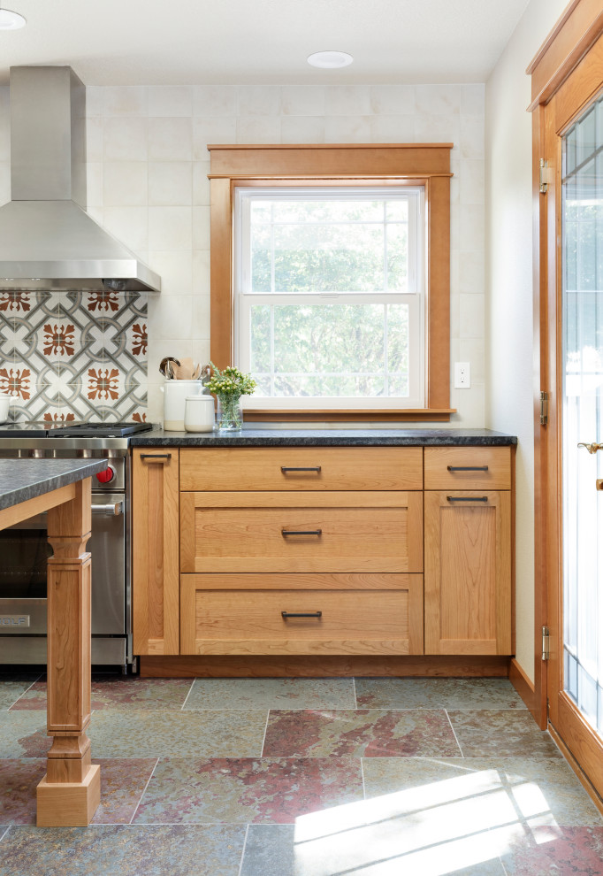 Inspiration for a mid-sized country u-shaped slate floor and multicolored floor enclosed kitchen remodel in Portland with a farmhouse sink, shaker cabinets, medium tone wood cabinets, granite countertops, white backsplash, ceramic backsplash, stainless steel appliances, an island and black countertops