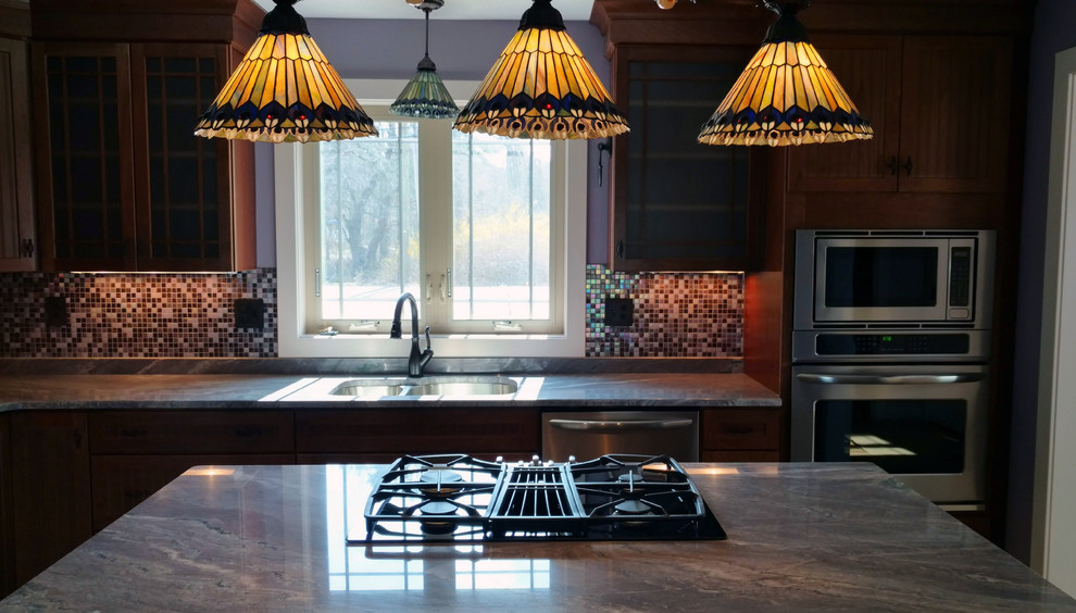 Bild på ett avskilt, mellanstort amerikanskt l-kök, med en undermonterad diskho, luckor med glaspanel, granitbänkskiva, flerfärgad stänkskydd, stänkskydd i glaskakel, rostfria vitvaror, en köksö och skåp i mellenmörkt trä
