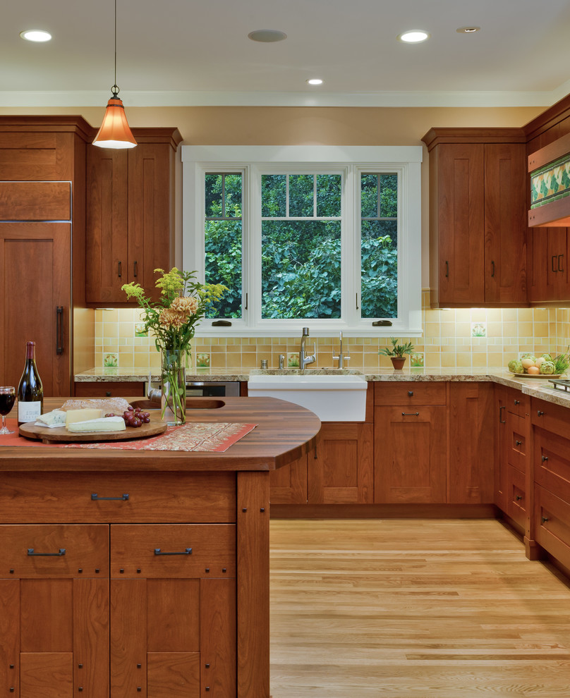 Foto på ett mycket stort amerikanskt kök, med en rustik diskho, skåp i shakerstil, skåp i mellenmörkt trä, granitbänkskiva, gult stänkskydd, stänkskydd i keramik, integrerade vitvaror, ljust trägolv och en köksö
