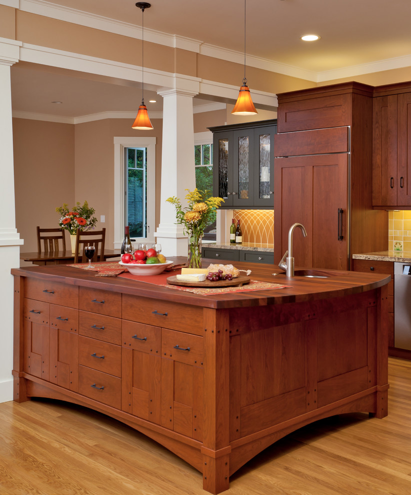 Exempel på ett mycket stort amerikanskt kök, med en rustik diskho, skåp i shakerstil, skåp i mellenmörkt trä, granitbänkskiva, gult stänkskydd, stänkskydd i keramik, integrerade vitvaror, ljust trägolv och en köksö