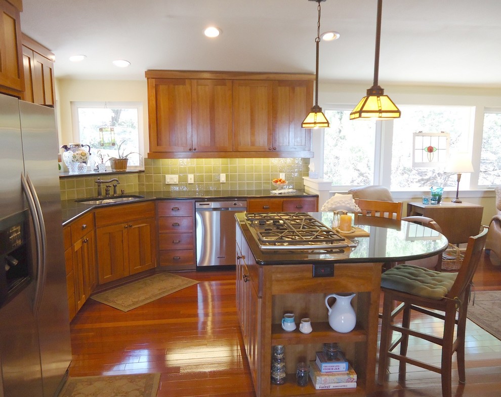 Amerikansk inredning av ett kök, med en undermonterad diskho, skåp i shakerstil, skåp i mellenmörkt trä, granitbänkskiva, grönt stänkskydd, mellanmörkt trägolv, en köksö, stänkskydd i terrakottakakel och rostfria vitvaror