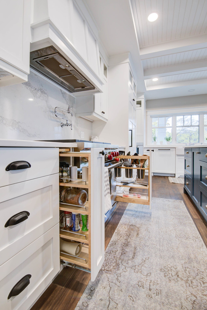 Enclosed kitchen - mid-sized craftsman single-wall medium tone wood floor and brown floor enclosed kitchen idea in Calgary with a farmhouse sink, shaker cabinets, blue cabinets, quartz countertops, white backsplash, stone slab backsplash, stainless steel appliances, an island and white countertops