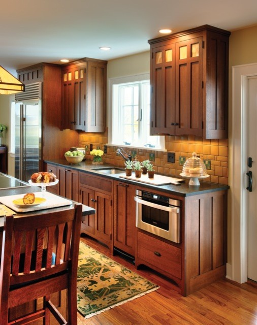 Exempel på ett mellanstort amerikanskt svart svart kök, med en undermonterad diskho, luckor med infälld panel, skåp i mellenmörkt trä, bänkskiva i täljsten, gult stänkskydd, stänkskydd i keramik, rostfria vitvaror, mellanmörkt trägolv, en köksö och brunt golv
