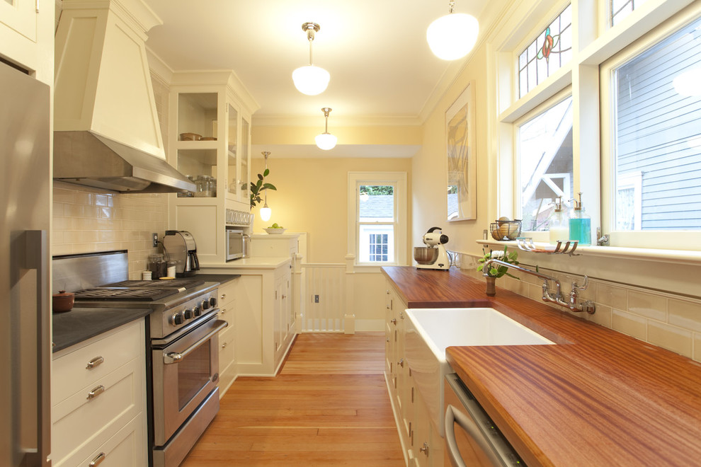 Example of an arts and crafts galley enclosed kitchen design in Portland with shaker cabinets, stainless steel appliances, a farmhouse sink, wood countertops, white backsplash and subway tile backsplash