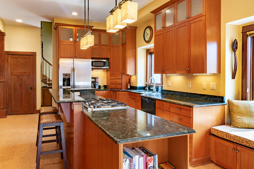 Exempel på ett stort amerikanskt grön grönt l-kök, med en undermonterad diskho, skåp i shakerstil, skåp i mellenmörkt trä, granitbänkskiva, rostfria vitvaror, korkgolv och en köksö