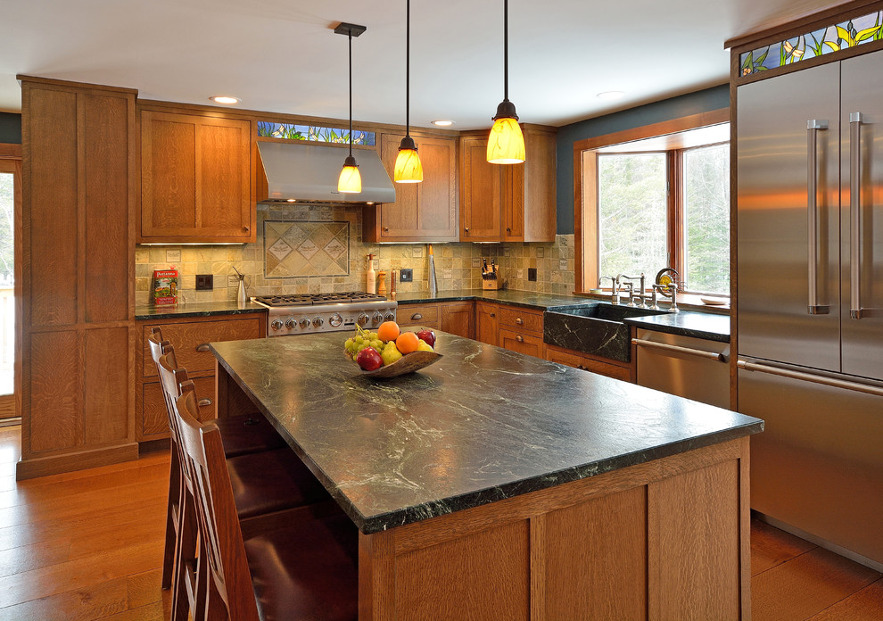 Example of an arts and crafts l-shaped medium tone wood floor eat-in kitchen design in Portland Maine with a farmhouse sink, shaker cabinets, medium tone wood cabinets and stainless steel appliances