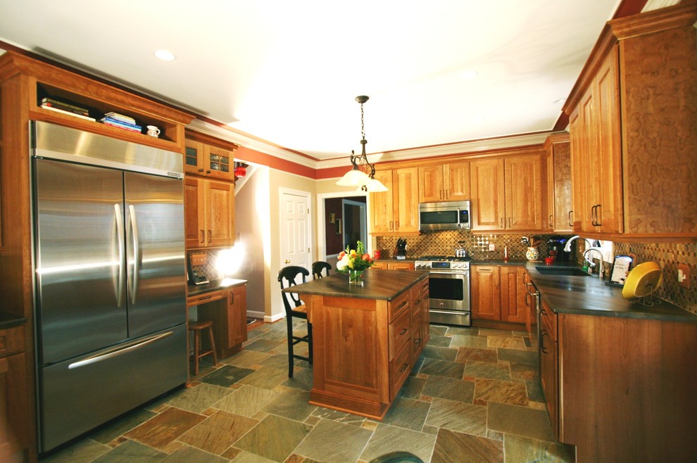 Amerikansk inredning av ett avskilt, stort u-kök, med en undermonterad diskho, luckor med upphöjd panel, skåp i mellenmörkt trä, bänkskiva i täljsten, brunt stänkskydd, stänkskydd i mosaik, rostfria vitvaror och en köksö