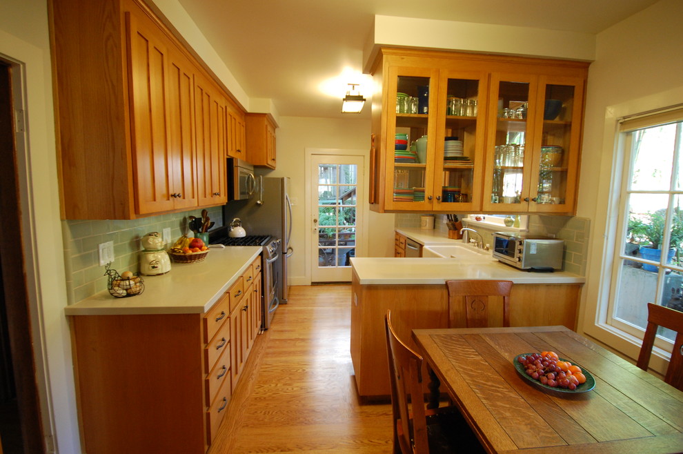 This is an example of a medium sized traditional u-shaped kitchen/diner in San Francisco with a belfast sink, recessed-panel cabinets, medium wood cabinets, engineered stone countertops, green splashback, ceramic splashback, stainless steel appliances and medium hardwood flooring.