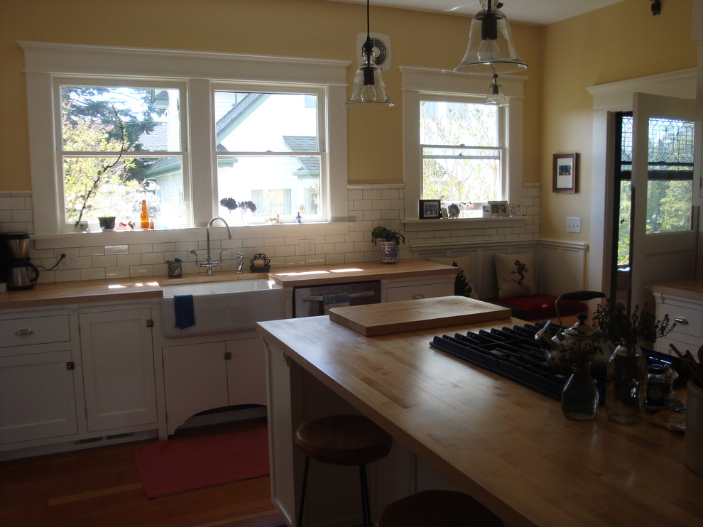 This is an example of a small classic enclosed kitchen in Seattle with a belfast sink, shaker cabinets, white cabinets, wood worktops, white splashback, stainless steel appliances, medium hardwood flooring, a breakfast bar, brown floors, beige worktops and metro tiled splashback.
