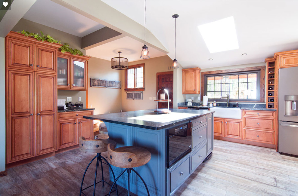 Bild på ett stort amerikanskt svart svart kök, med en rustik diskho, luckor med profilerade fronter, skåp i mellenmörkt trä, granitbänkskiva, blått stänkskydd, stänkskydd i glaskakel, rostfria vitvaror, mellanmörkt trägolv, en köksö och brunt golv