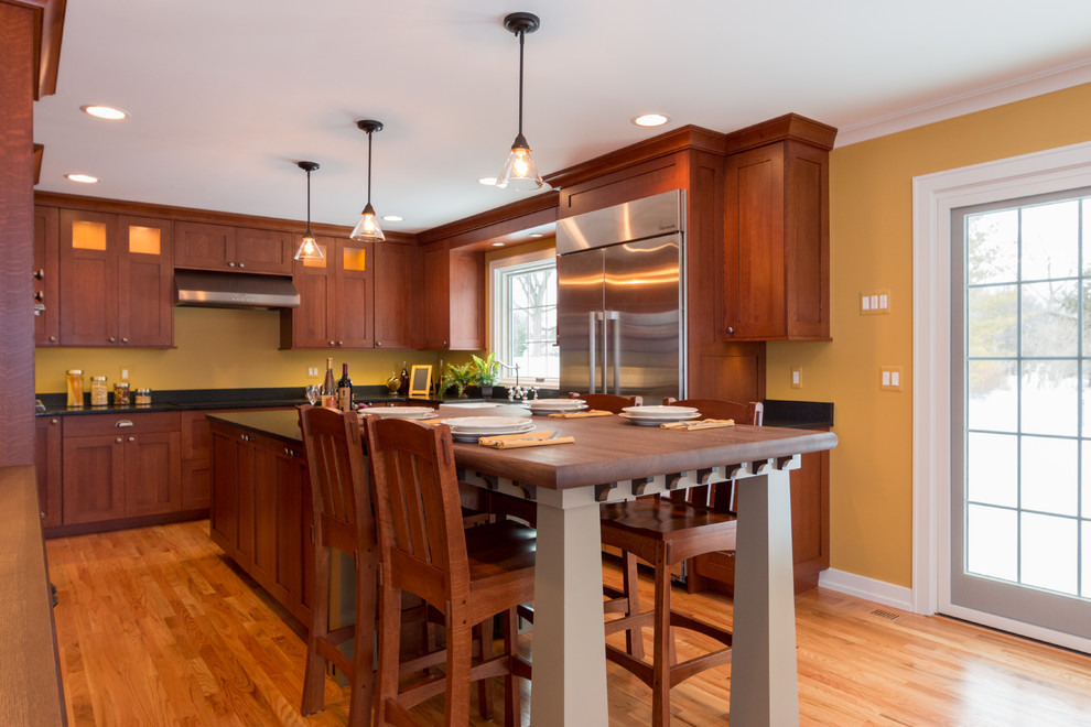 Example of a large arts and crafts u-shaped light wood floor eat-in kitchen design in Detroit with a farmhouse sink, flat-panel cabinets, medium tone wood cabinets, granite countertops, yellow backsplash, stainless steel appliances and an island