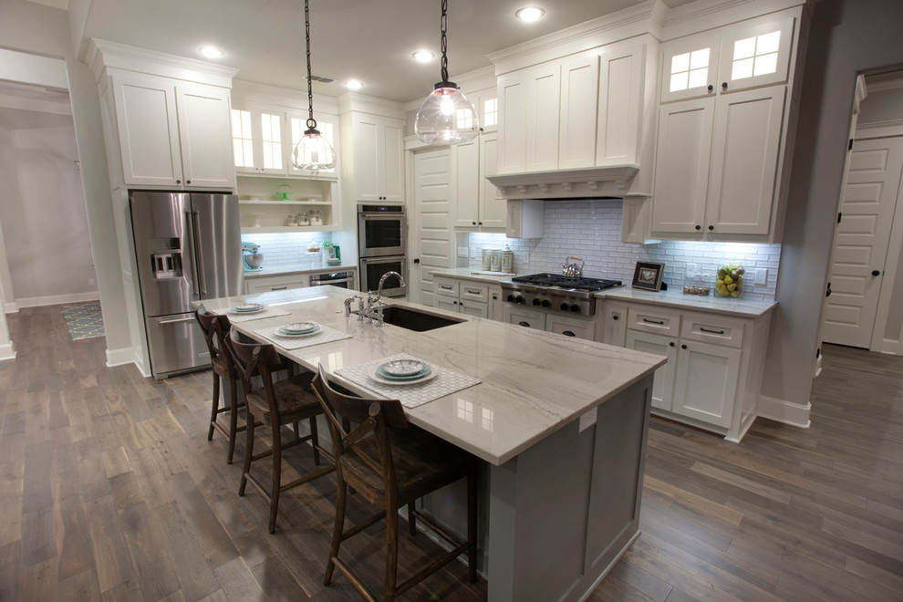 Bild på ett stort amerikanskt kök, med en nedsänkt diskho, skåp i shakerstil, vita skåp, bänkskiva i kvartsit, vitt stänkskydd, stänkskydd i keramik, rostfria vitvaror, mellanmörkt trägolv och en köksö