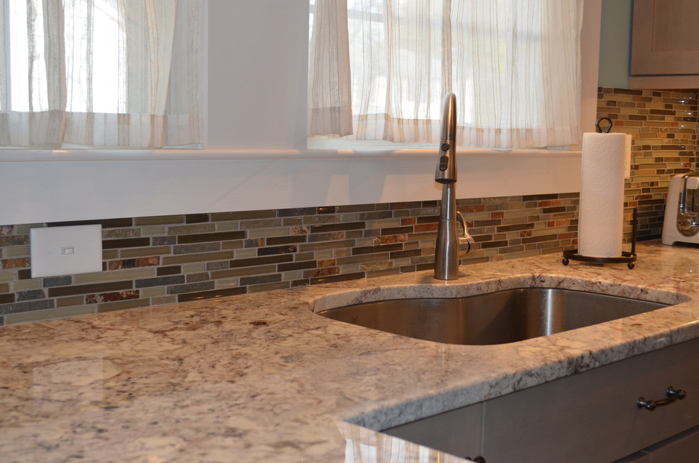 Bild på ett avskilt, litet amerikanskt u-kök, med en undermonterad diskho, luckor med infälld panel, grå skåp, granitbänkskiva, flerfärgad stänkskydd, stänkskydd i glaskakel, rostfria vitvaror, vinylgolv och brunt golv