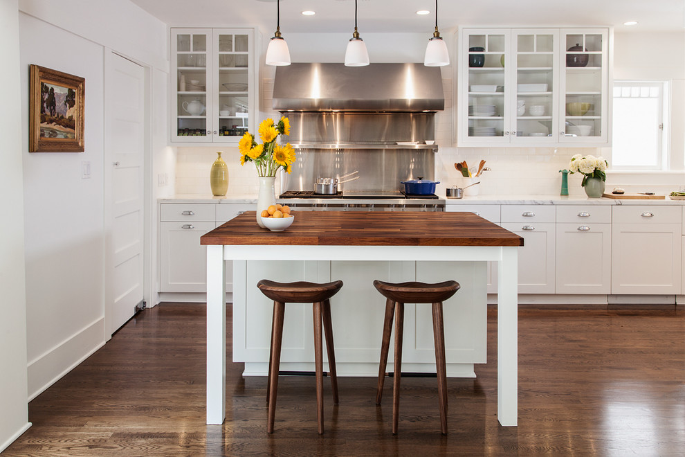 Modelo de cocina clásica con armarios estilo shaker, puertas de armario blancas, salpicadero blanco, salpicadero de azulejos tipo metro, suelo de madera oscura y una isla