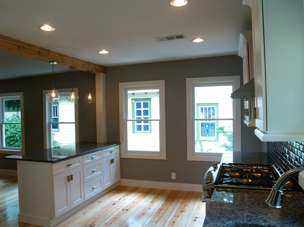 Example of a mid-sized arts and crafts galley light wood floor open concept kitchen design in Atlanta with an undermount sink, recessed-panel cabinets, white cabinets, granite countertops, gray backsplash, glass tile backsplash, stainless steel appliances and a peninsula