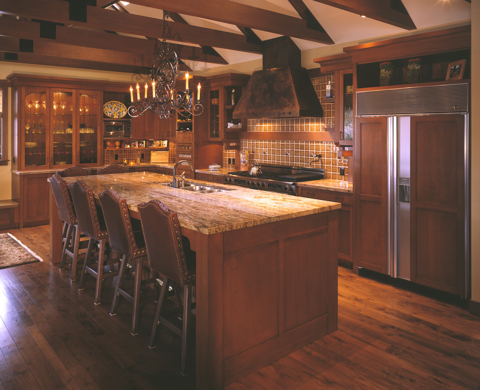 Foto på ett amerikanskt kök, med en trippel diskho, skåp i shakerstil, skåp i mellenmörkt trä, granitbänkskiva, brunt stänkskydd, stänkskydd i porslinskakel, integrerade vitvaror, mellanmörkt trägolv och en köksö