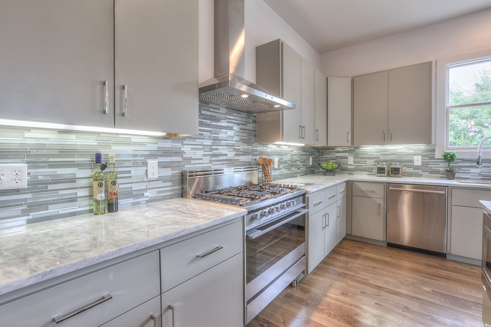 This is an example of a large classic l-shaped open plan kitchen in Nashville with a double-bowl sink, flat-panel cabinets, grey cabinets, quartz worktops, grey splashback, matchstick tiled splashback, stainless steel appliances, medium hardwood flooring and an island.