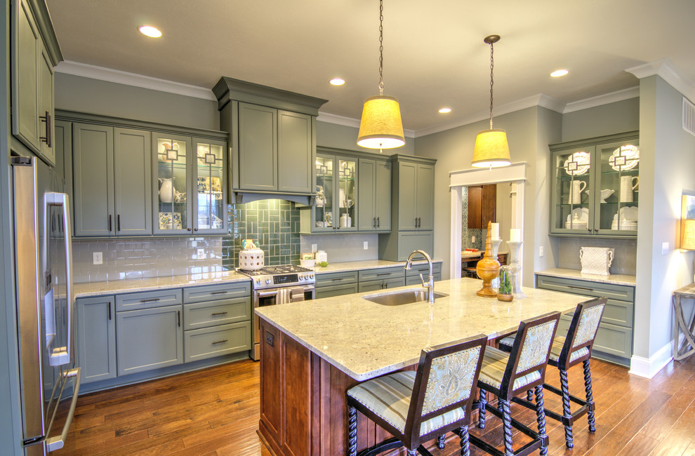 Elegant l-shaped medium tone wood floor kitchen photo in Indianapolis with an undermount sink, shaker cabinets, green cabinets, gray backsplash, stainless steel appliances and an island