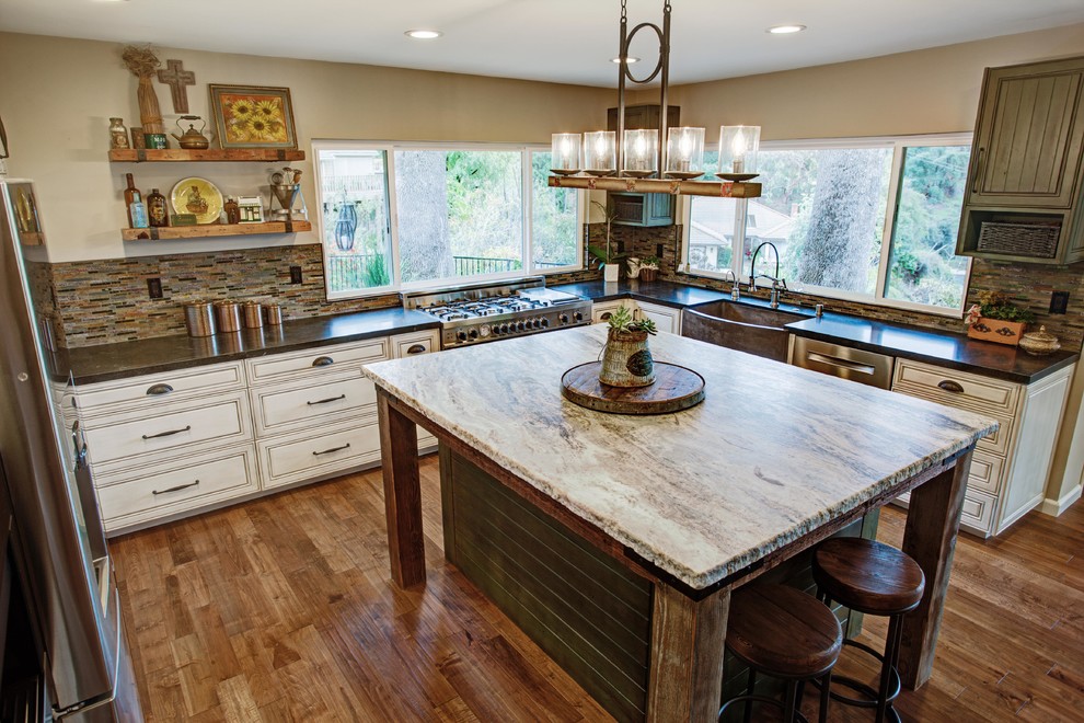 This is an example of a large traditional u-shaped open plan kitchen in Los Angeles with a belfast sink, raised-panel cabinets, distressed cabinets, granite worktops, brown splashback, ceramic splashback, stainless steel appliances, medium hardwood flooring and an island.