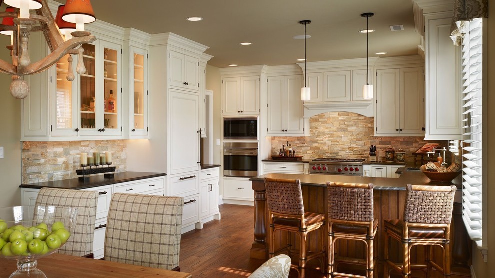 Exempel på ett stort amerikanskt u-kök, med en undermonterad diskho, luckor med infälld panel, vita skåp, marmorbänkskiva, brunt stänkskydd, stänkskydd i stenkakel, rostfria vitvaror, mellanmörkt trägolv och en köksö