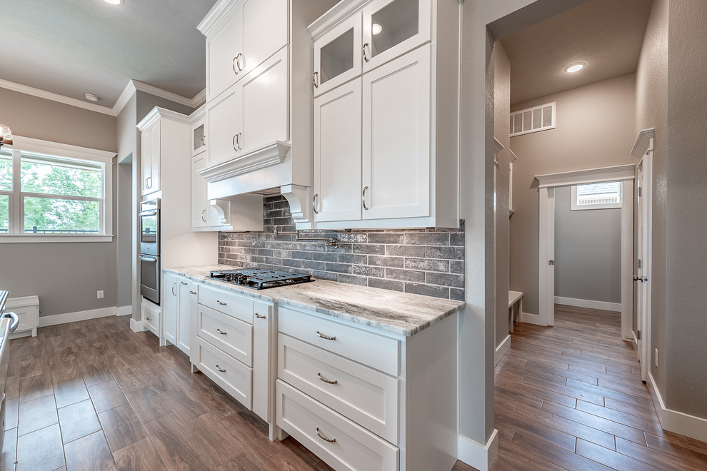Eat-in kitchen - large craftsman ceramic tile and brown floor eat-in kitchen idea in Other with a farmhouse sink, shaker cabinets, white cabinets, wood countertops, gray backsplash, brick backsplash, stainless steel appliances, an island and beige countertops