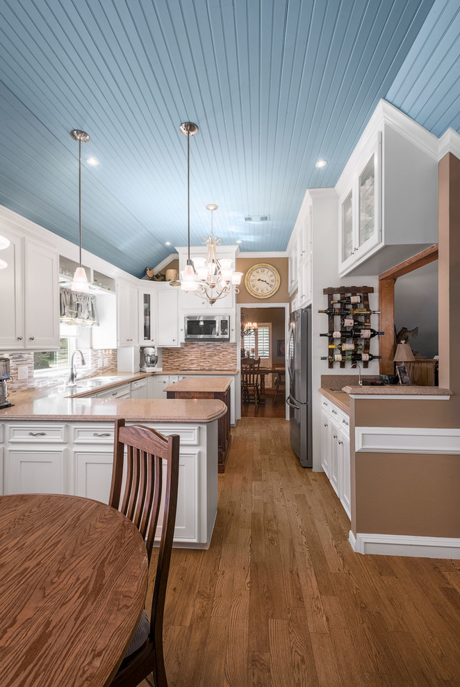 Design ideas for a medium sized classic u-shaped kitchen/diner in Houston with a double-bowl sink, white cabinets, marble worktops, beige splashback, glass tiled splashback, stainless steel appliances, light hardwood flooring, an island, brown floors and recessed-panel cabinets.