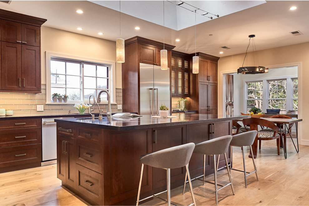 Example of a transitional galley light wood floor and beige floor kitchen design in San Francisco with recessed-panel cabinets, dark wood cabinets, stainless steel appliances, an island and brown countertops