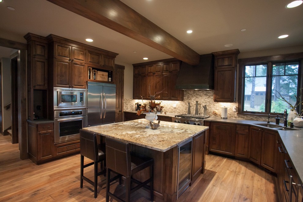 Example of an arts and crafts u-shaped medium tone wood floor eat-in kitchen design in Seattle with medium tone wood cabinets, solid surface countertops, gray backsplash, stone tile backsplash, stainless steel appliances, an undermount sink, raised-panel cabinets and an island